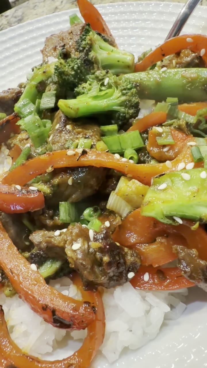 Close-up of beef and broccoli stir-fry with bell pepper and sesame seeds over rice