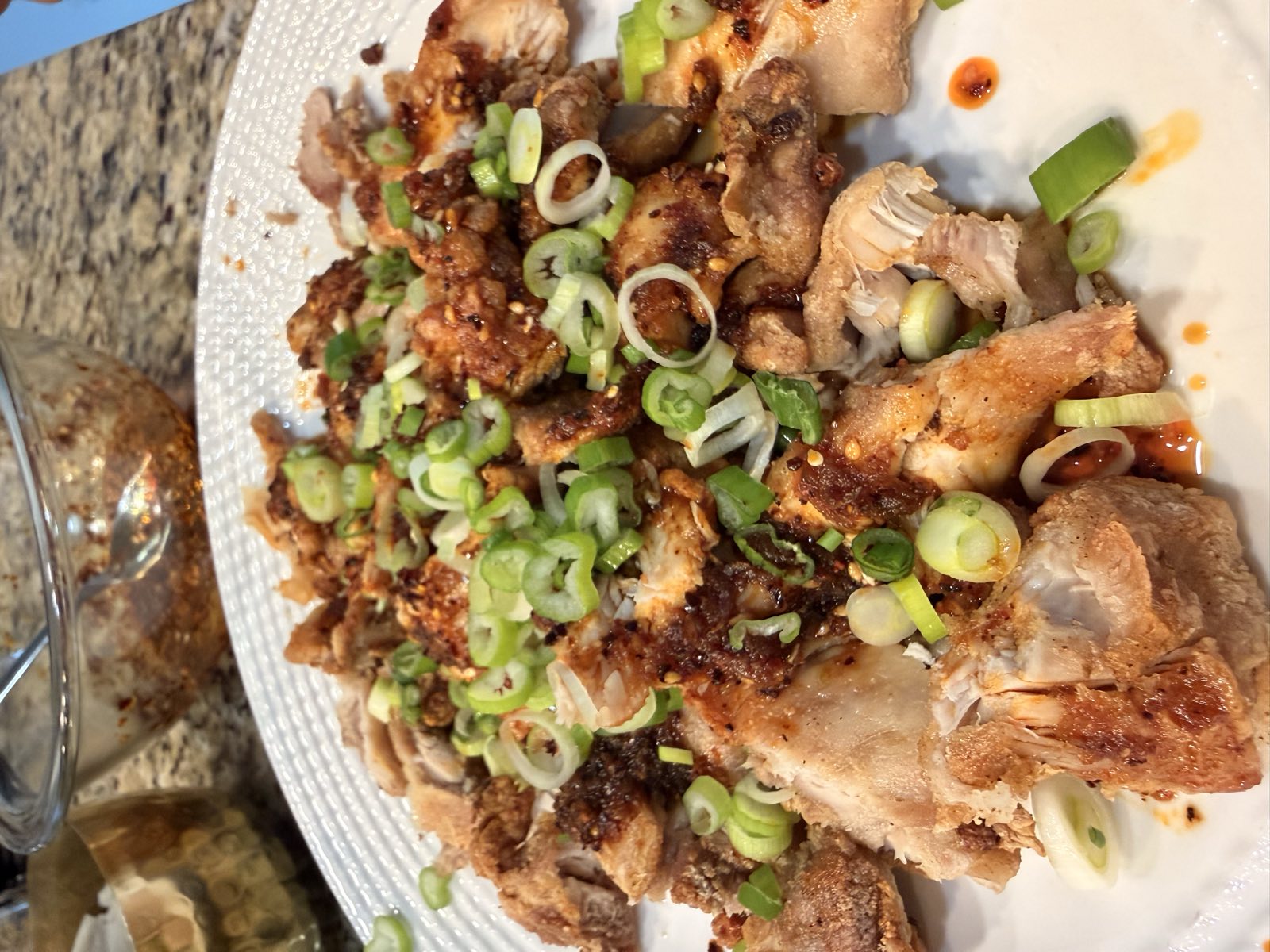 Crispy Szechuan chicken strips on a white plate, scattered with scallions and pooled chili oil