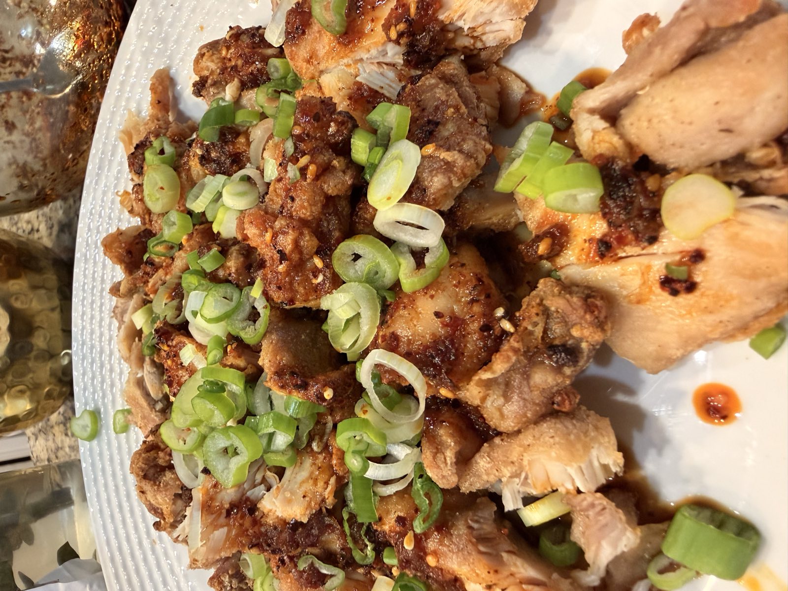 Crispy Szechuan chicken strips topped with sliced scallions, sesame seeds, and chili oil on a white plate
