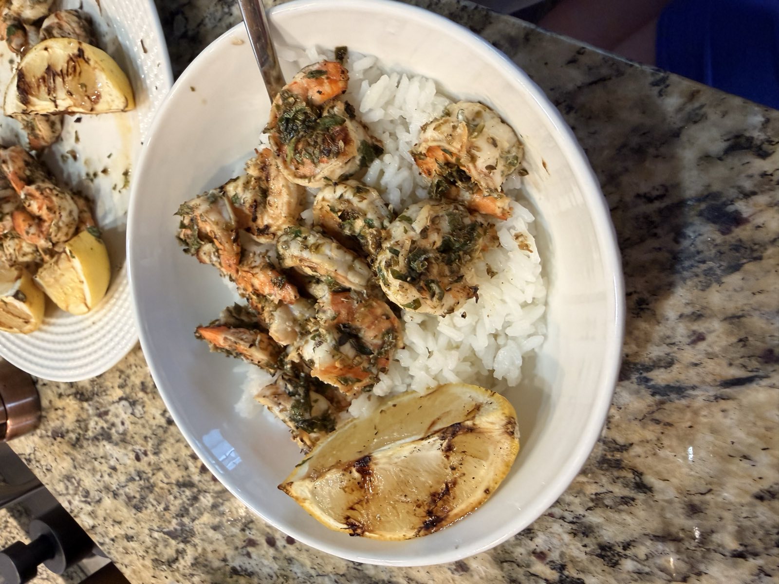Grilled lemon garlic shrimp piled over rice in a bowl with a grilled lemon wedge