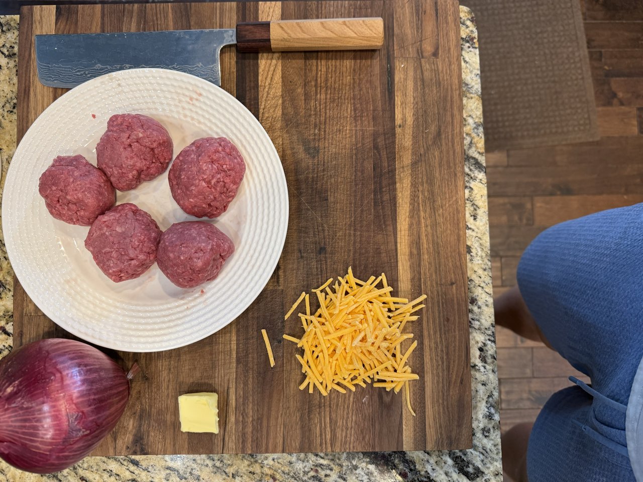 Beef balls, shredded sharp cheddar, butter, and a purple onion on a cutting board
