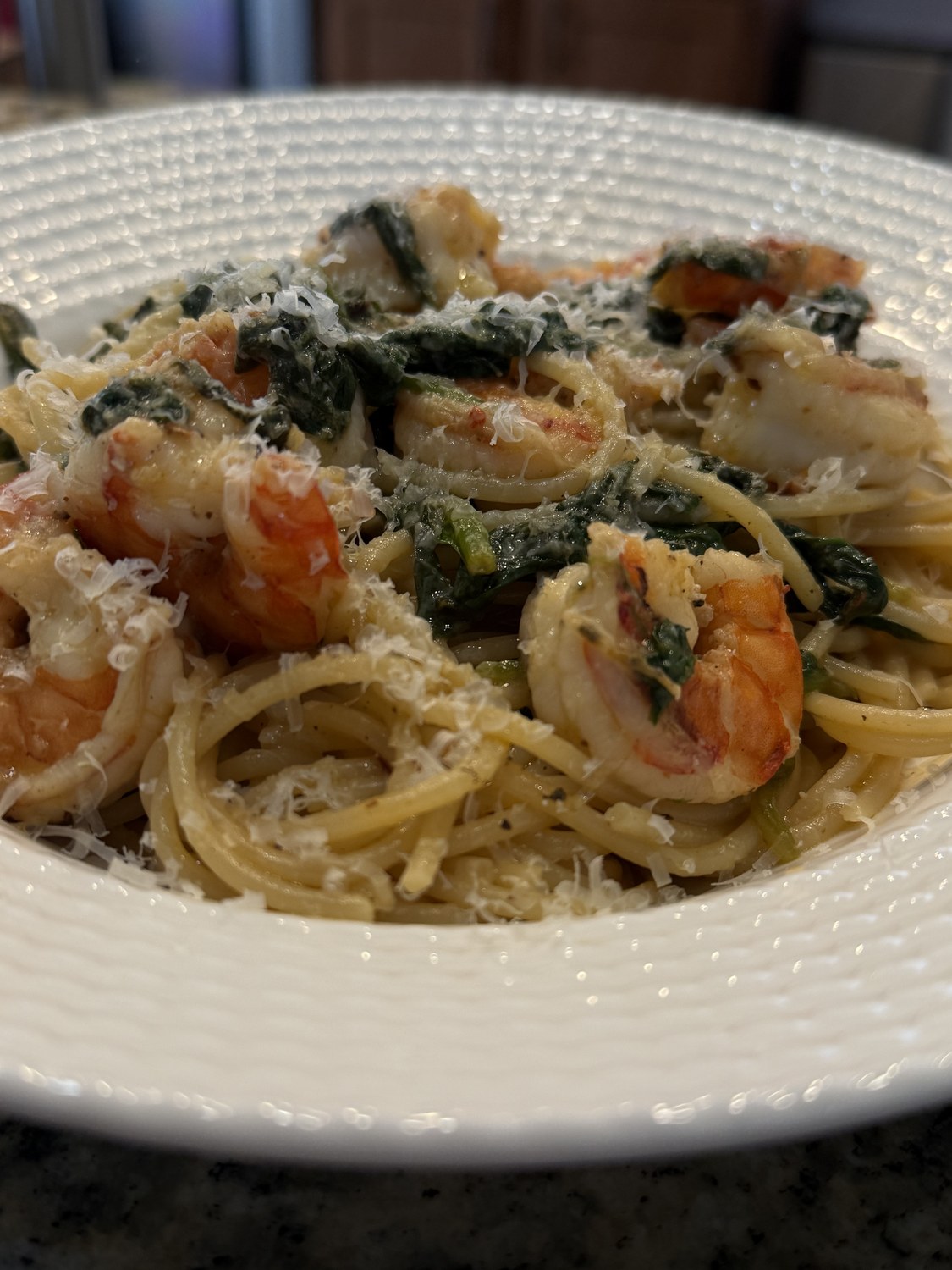 Cast-iron seared shrimp tossed with spaghetti, wilted spinach and grated parmesan in a white bowl