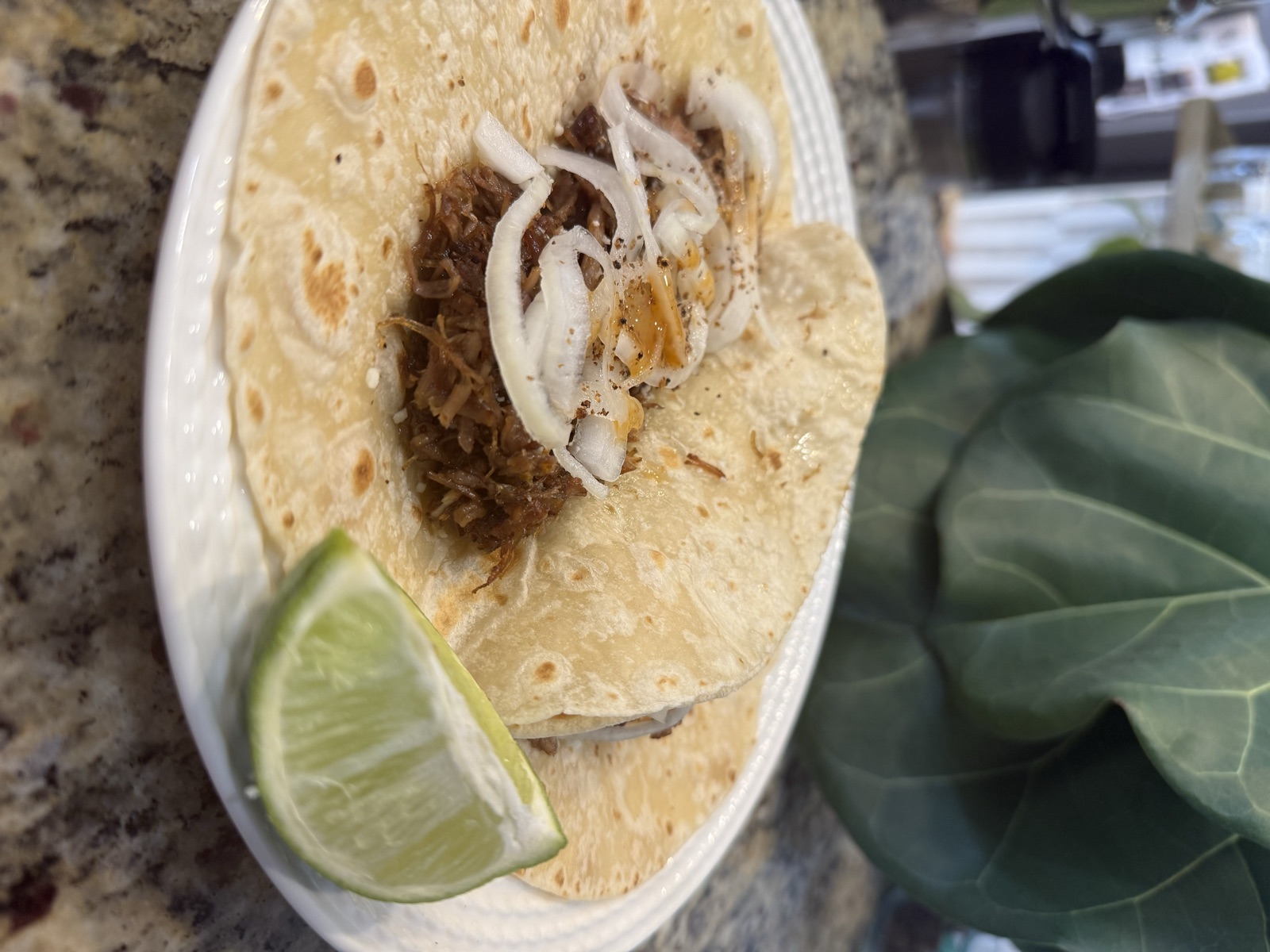A warm tortilla filled with crispy carnitas, pickled red onions, and cilantro with a lime wedge