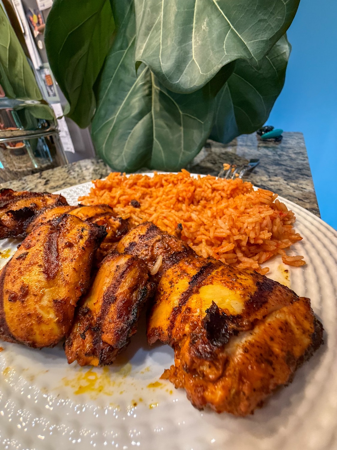 Grilled achiote chicken thighs with dark grill marks beside a serving of Mexican red rice on a white plate
