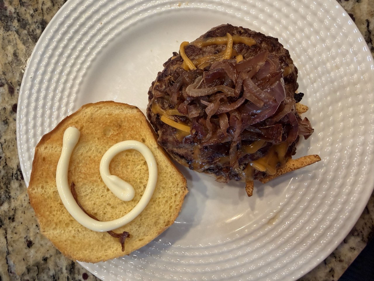 A smash burger with sharp cheddar and caramelized purple onions next to a toasted, mayo-swirled bun on a white plate